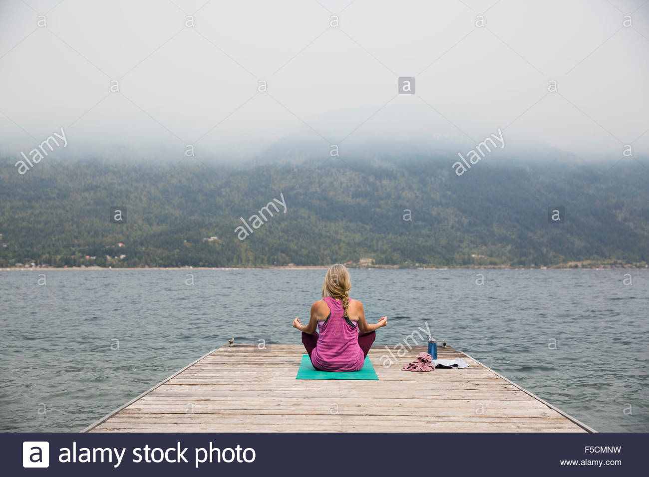Mature woman lotus position yoga mat overlooking lake Stock Photo