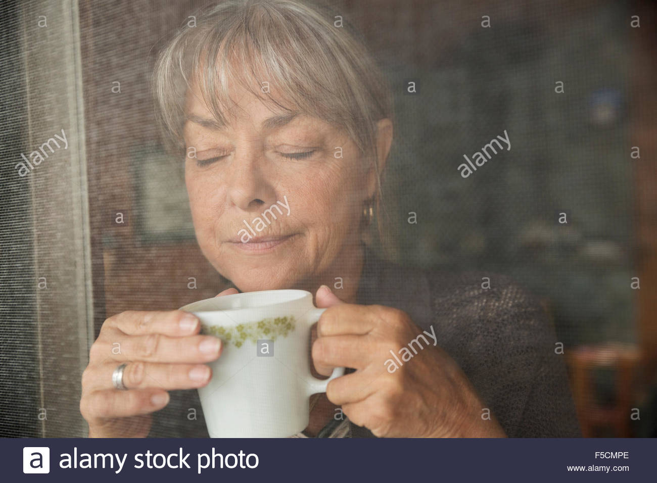Close up serene woman drinking coffee screen door Stock Photo