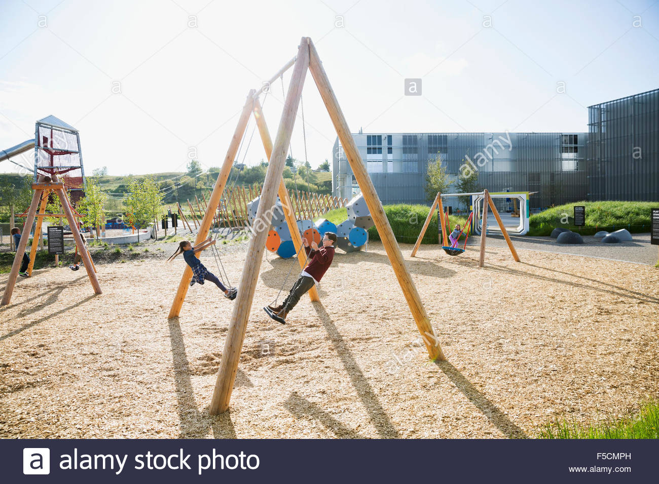 Kids playing on swings at sunny playground Stock Photo