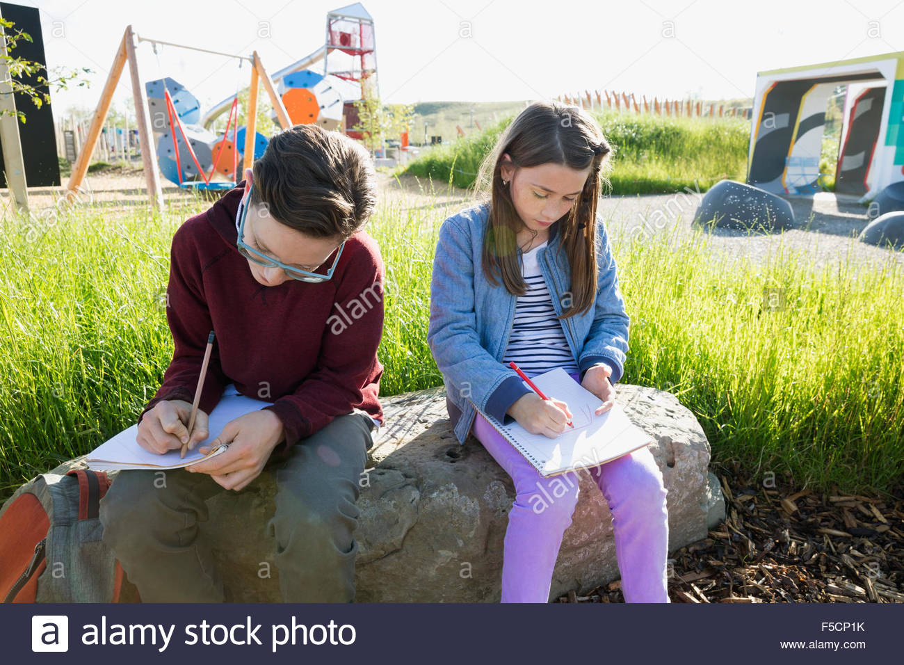 Students doing homework on rock near sunny playground Stock Photo