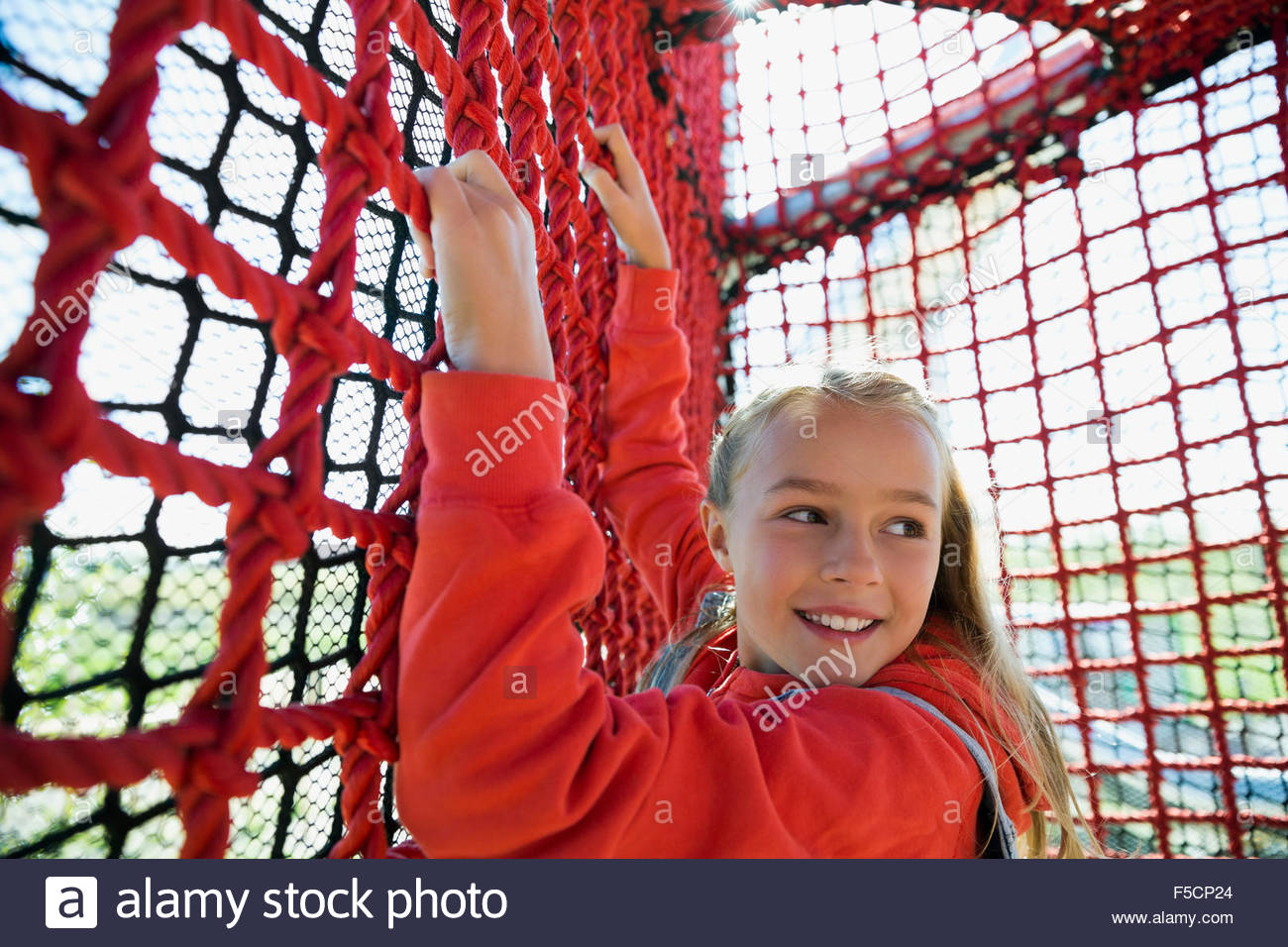 Girl hanging from rope net looking over shoulder Stock Photo