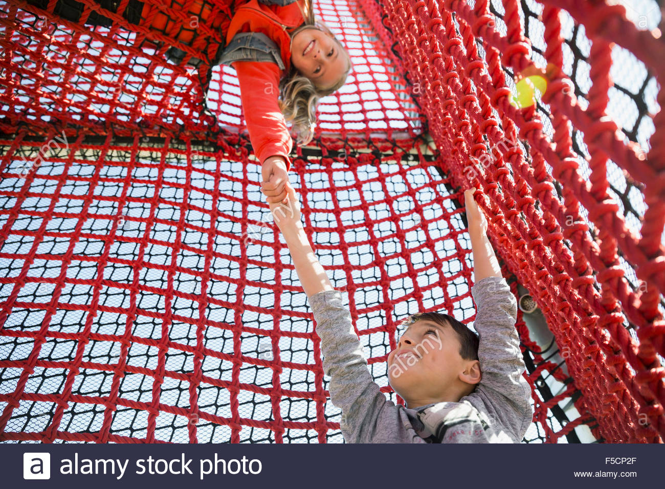 Girl lifting helping boy climb rope net Stock Photo Alamy