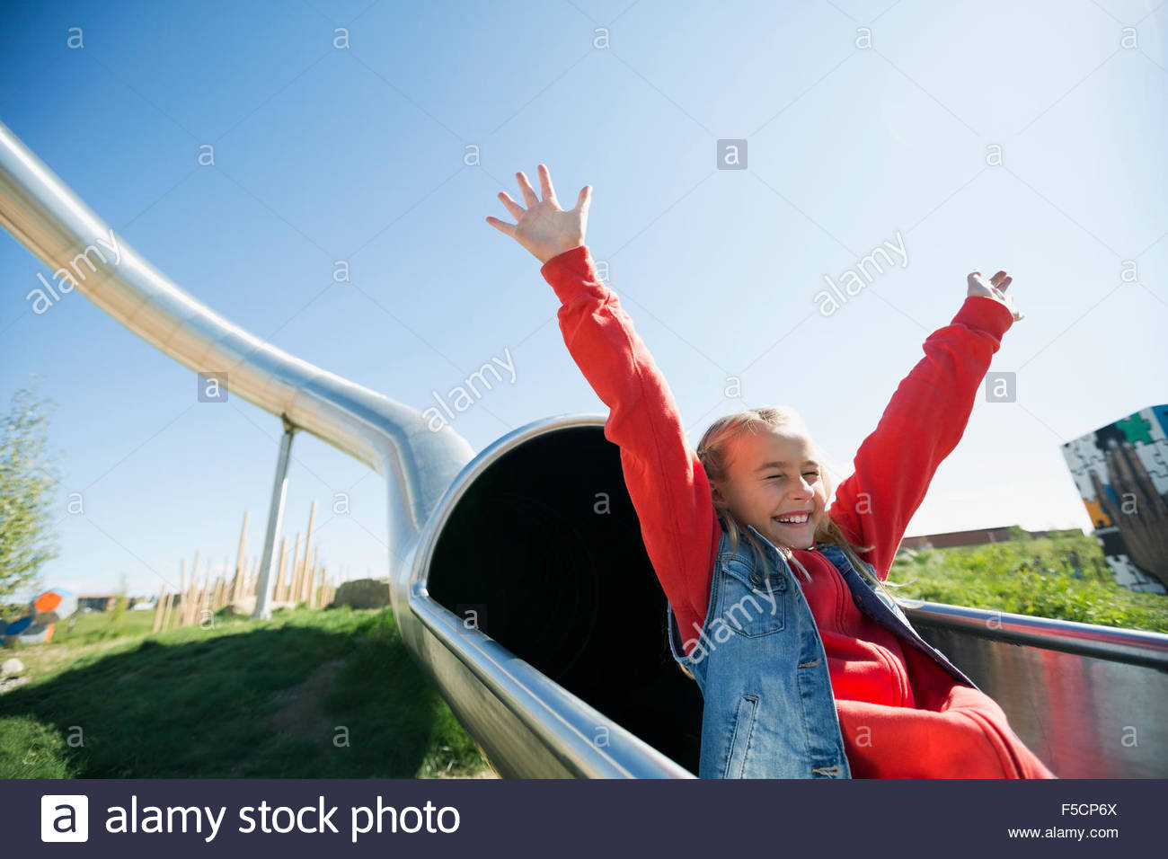 Carefree girl sliding from tunnel slide sunny playground Stock Photo