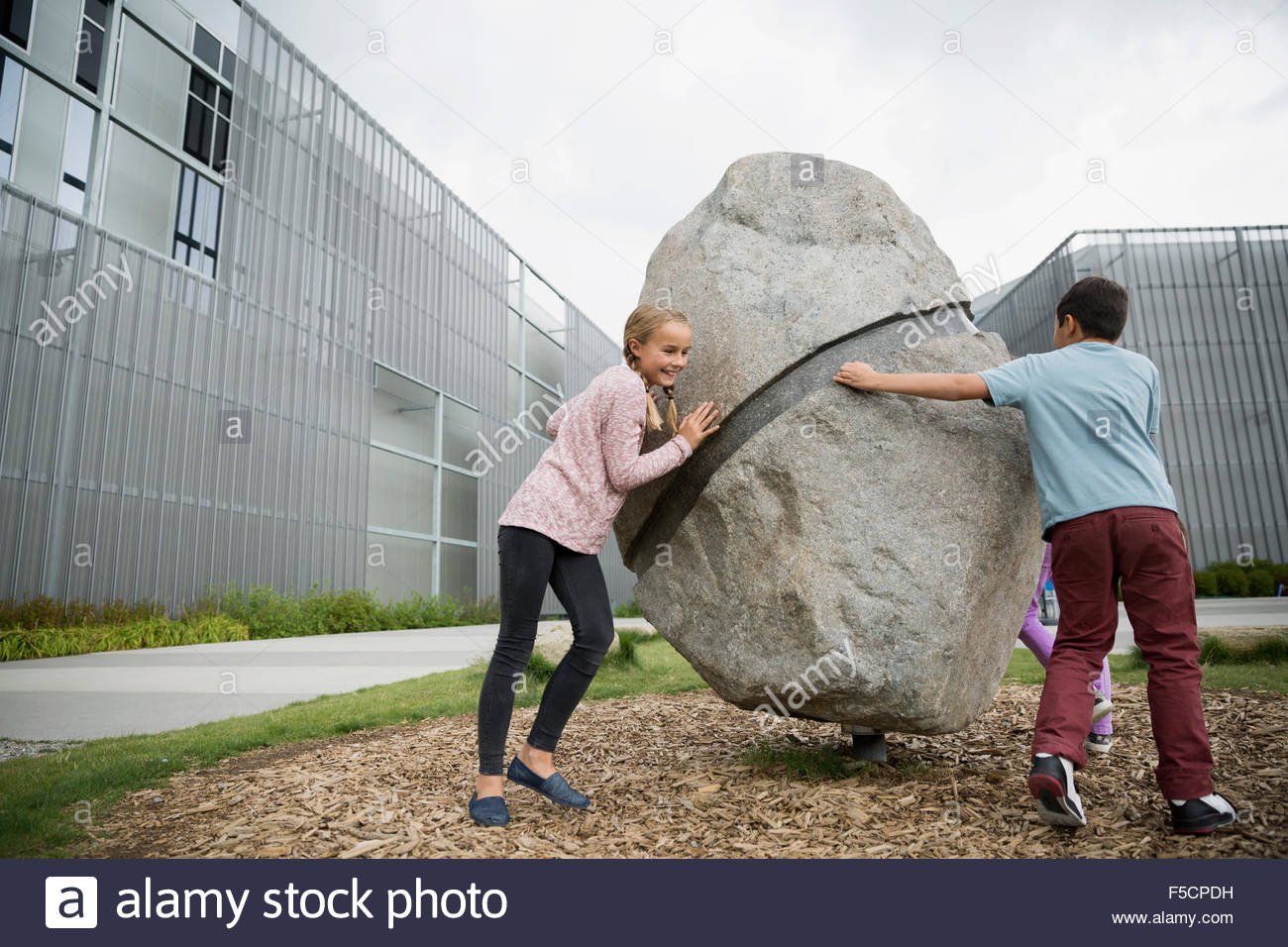 Boy and girl circling large boulder at playground Stock Photo