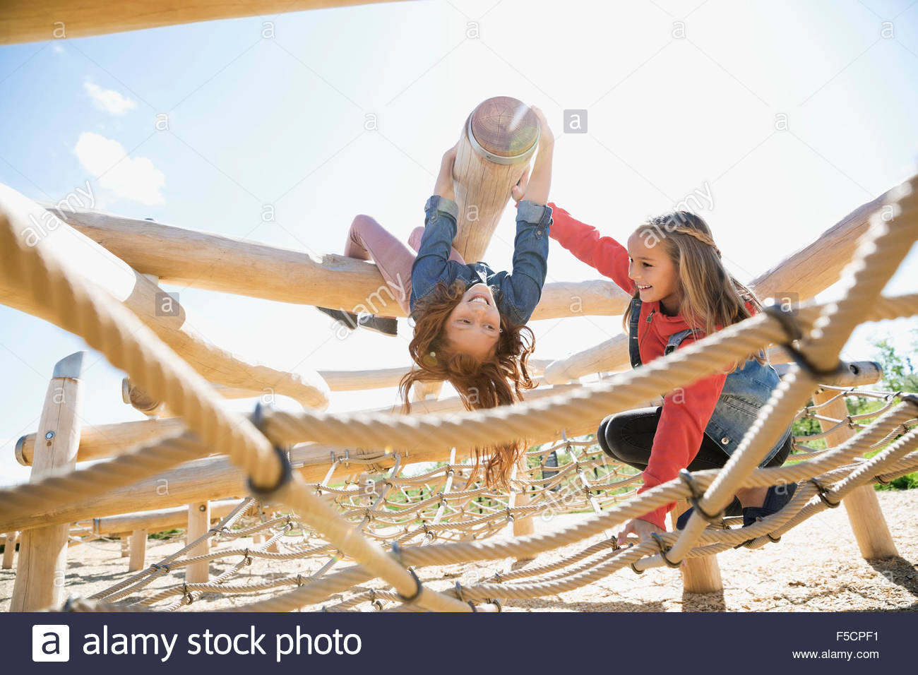 Girl hanging upside-down over net sunny playground Stock Photo