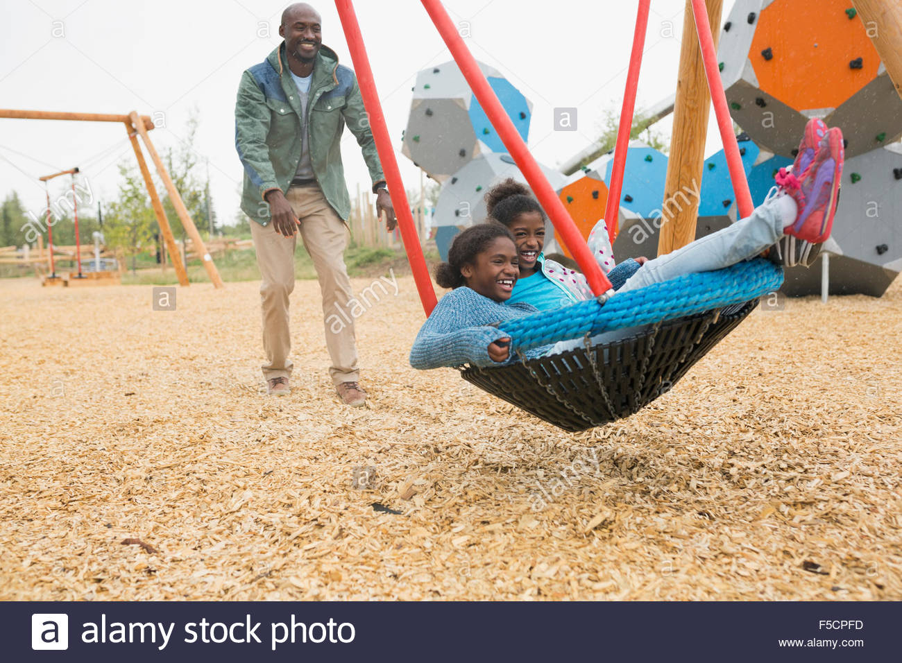Father pushing daughters in swing net at playground Stock Photo