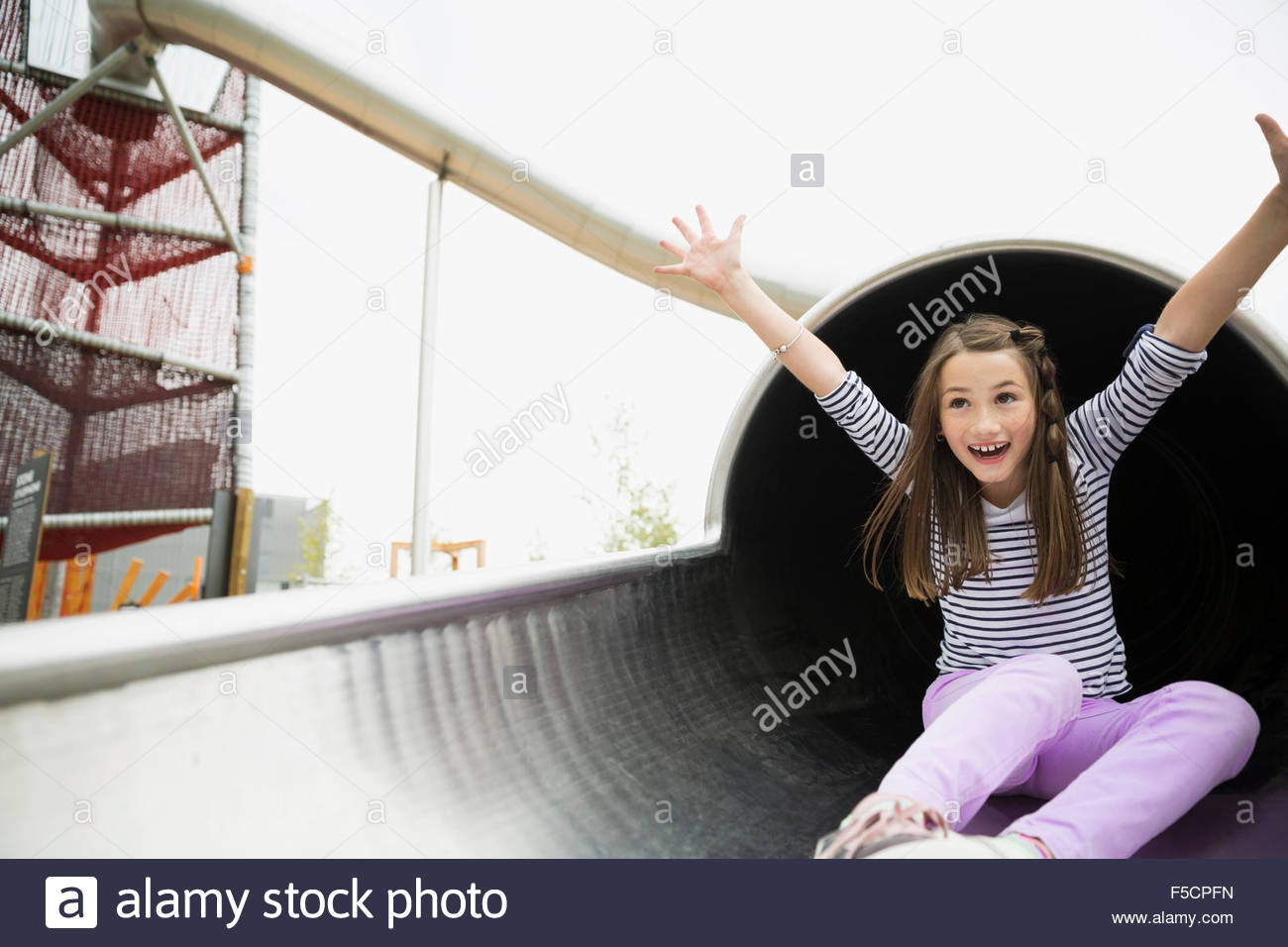Playful girl sliding out slide tunnel at playground Stock Photo