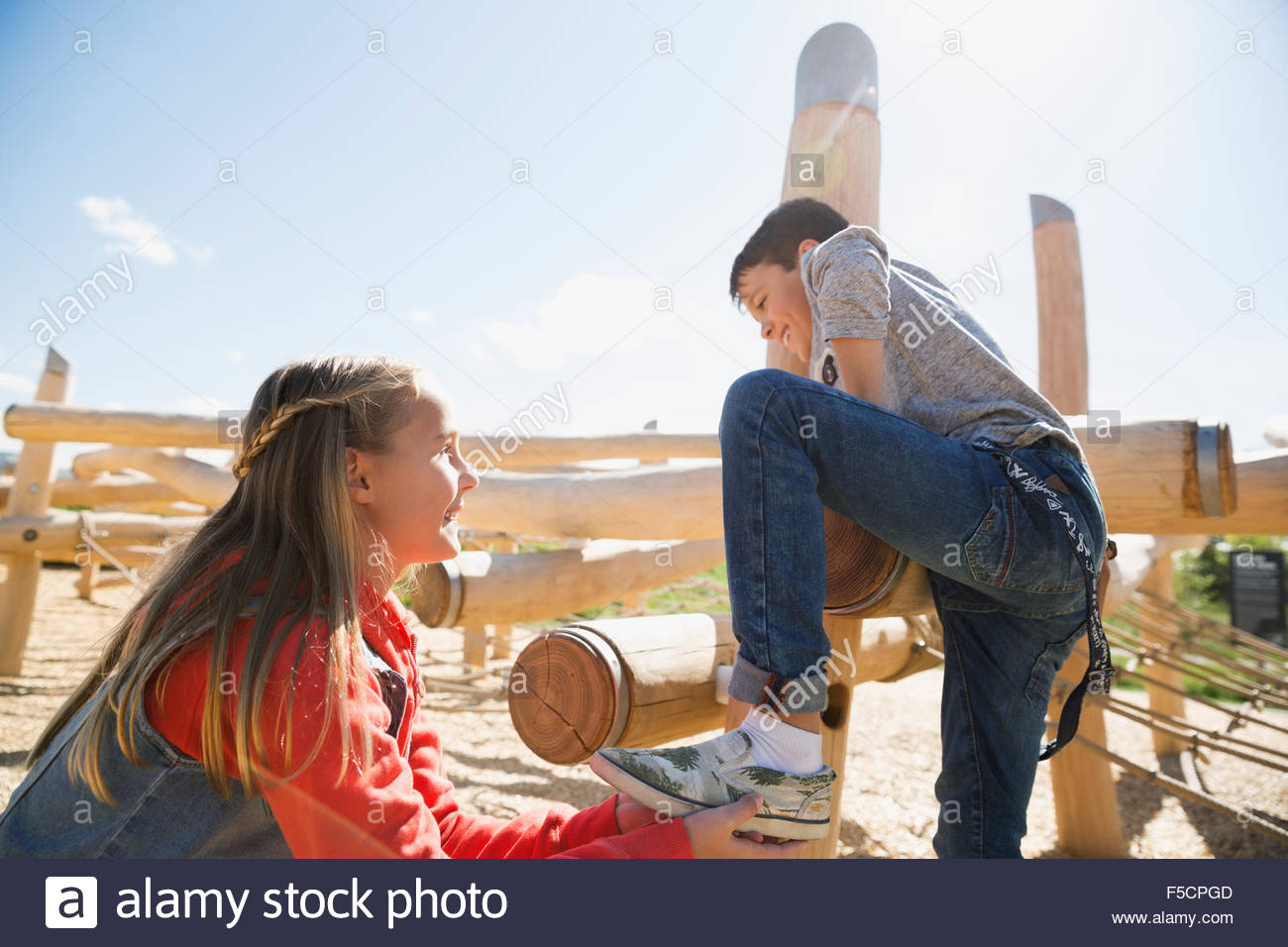Girl helping boy climb logs at sunny playground Stock Photo