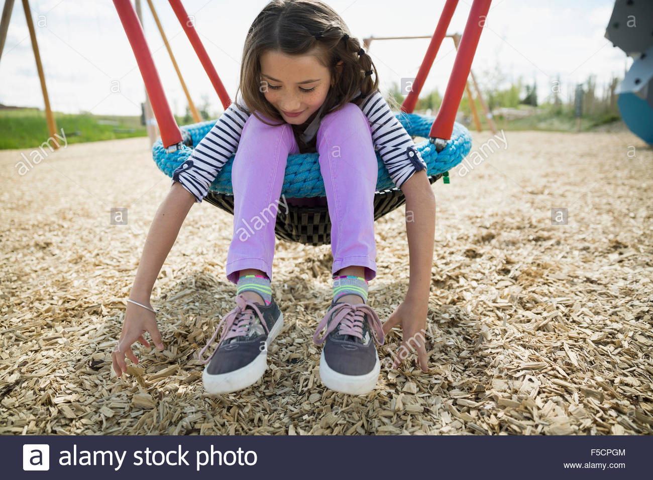 Girl sitting in swing looking down at playground Stock Photo