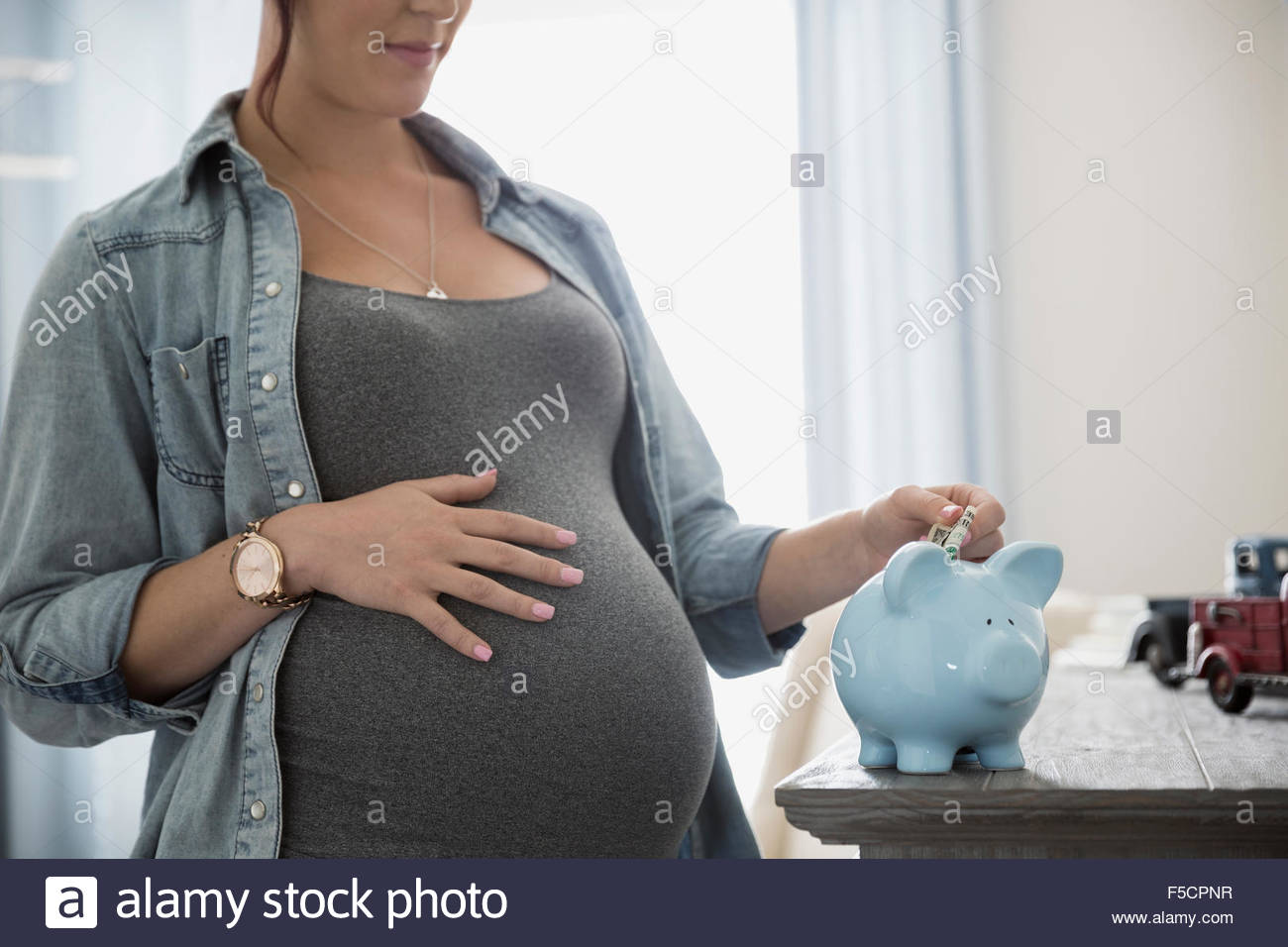 Pregnant woman depositing money into piggybank Stock Photo
