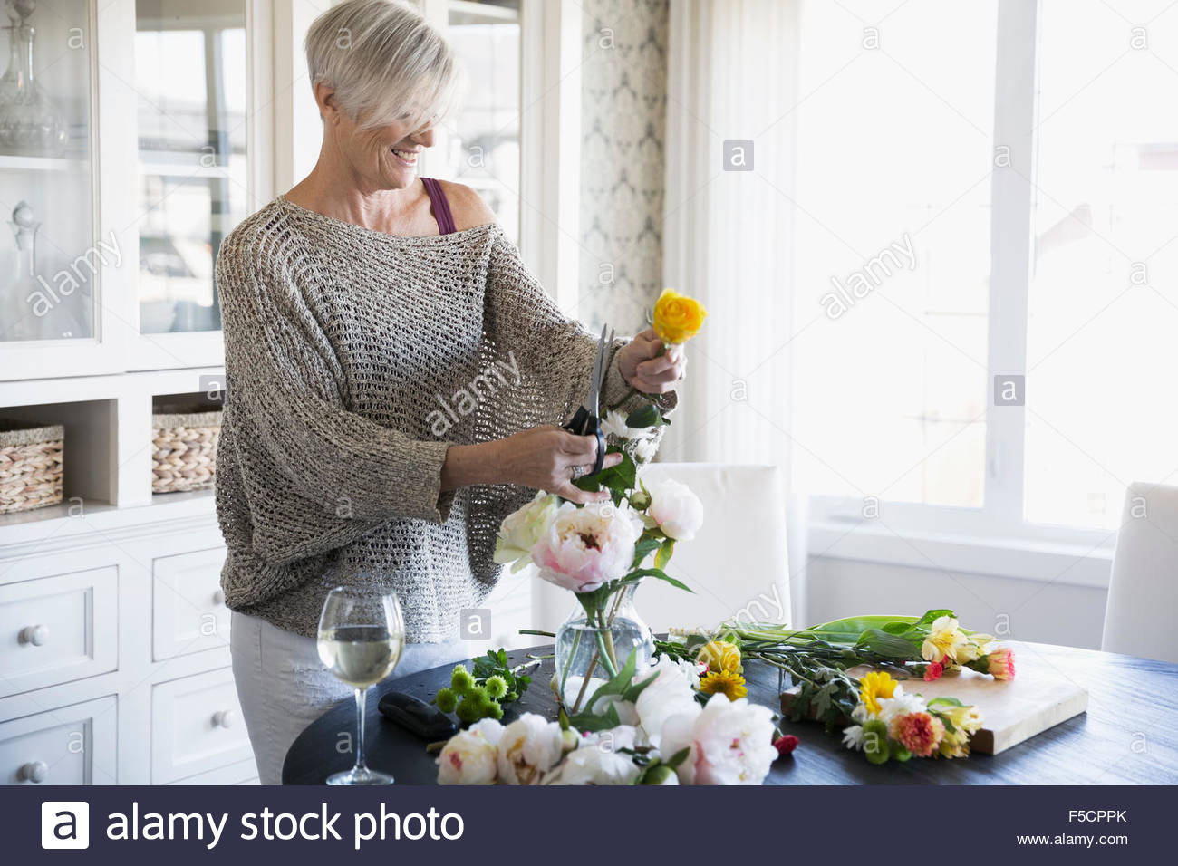 Woman arranging flowers and drinking wine Stock Photo