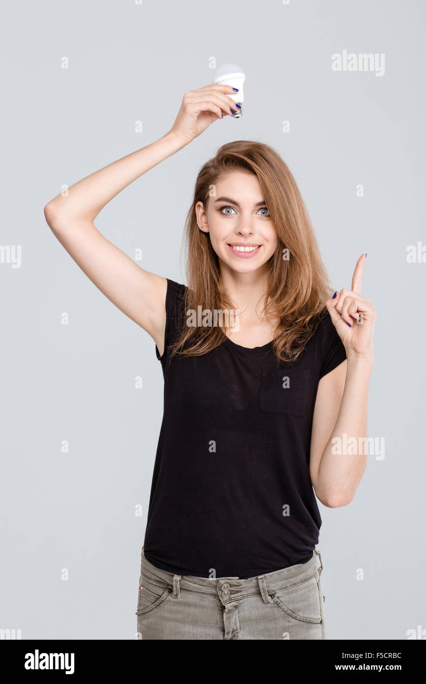 Portrait of a happy young woman holding light bulb over head and pointing finger up isolated on a white background Stock Photo