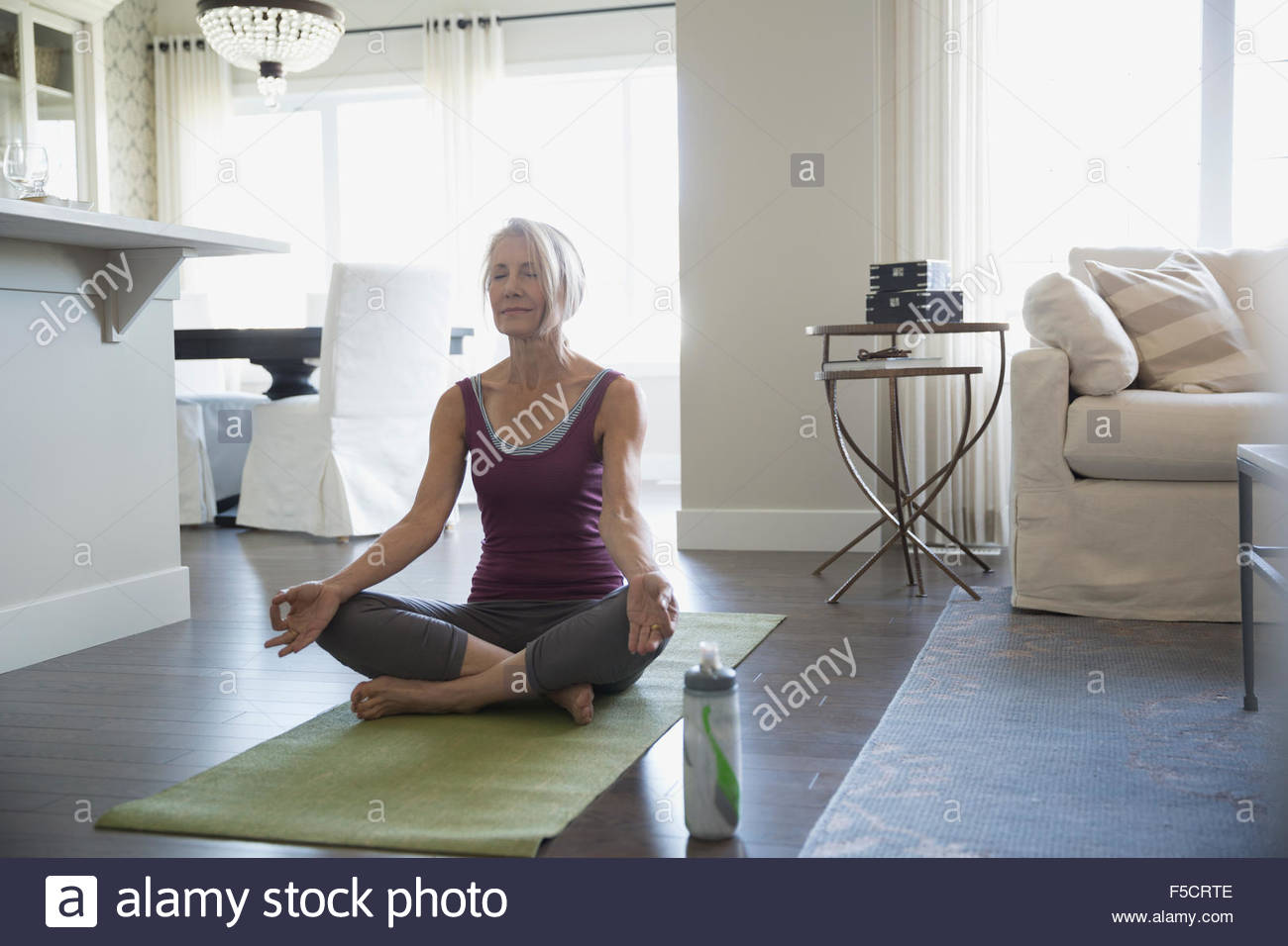 Serene senior woman meditating lotus position living room Stock Photo