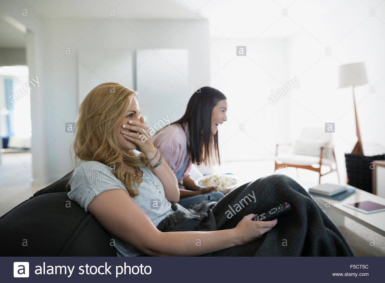 Laughing friends watching TV on living room sofa Stock Photo