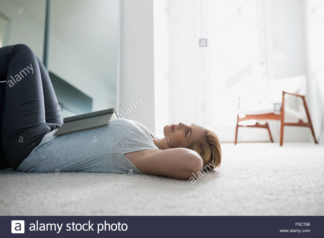 Serene woman with book, laying on bedroom floor Stock Photo