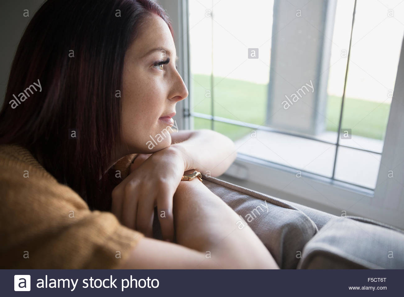 Pensive woman on sofa looking out window Stock Photo