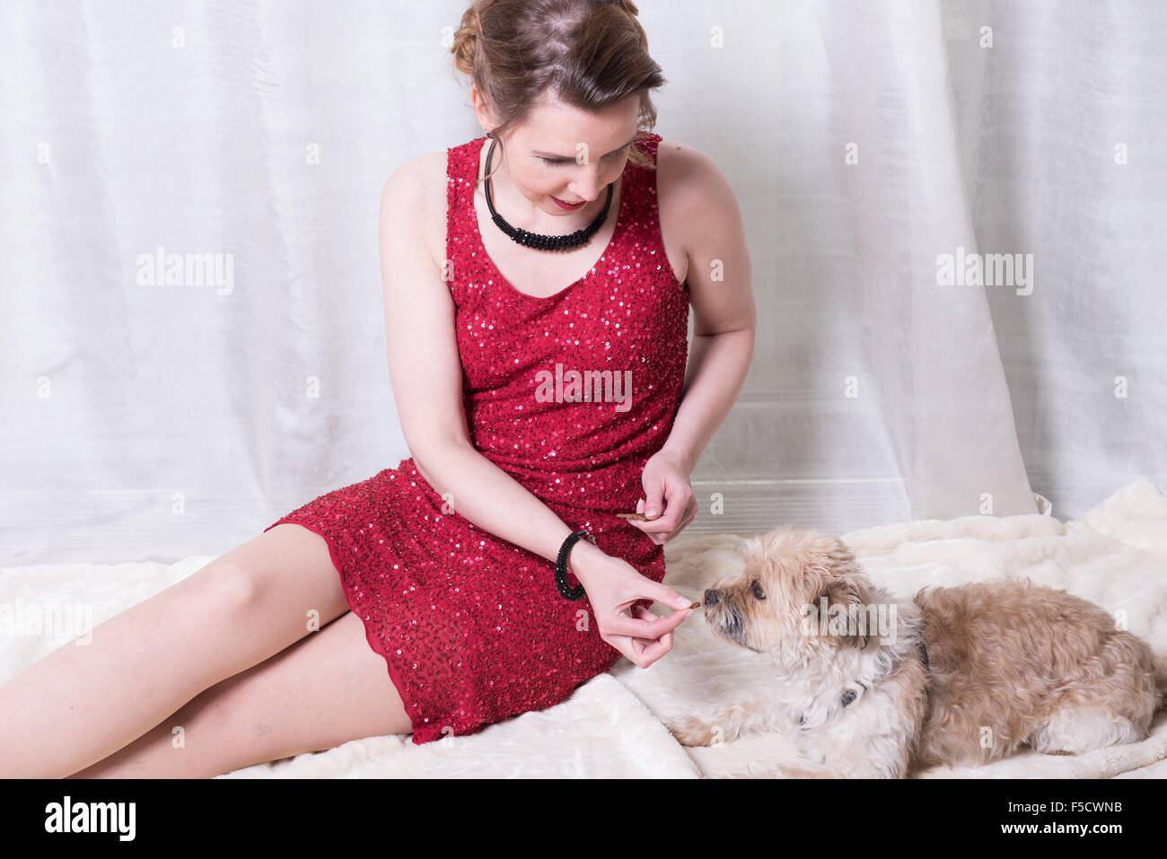 woman in red dress feeding dog on blanket Stock Photo