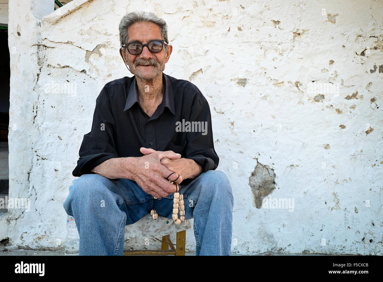 A man relaxes on the sidewalk with his worry beads in the mountain village of Anogia, on the island of Crete in Greece Stock Photo