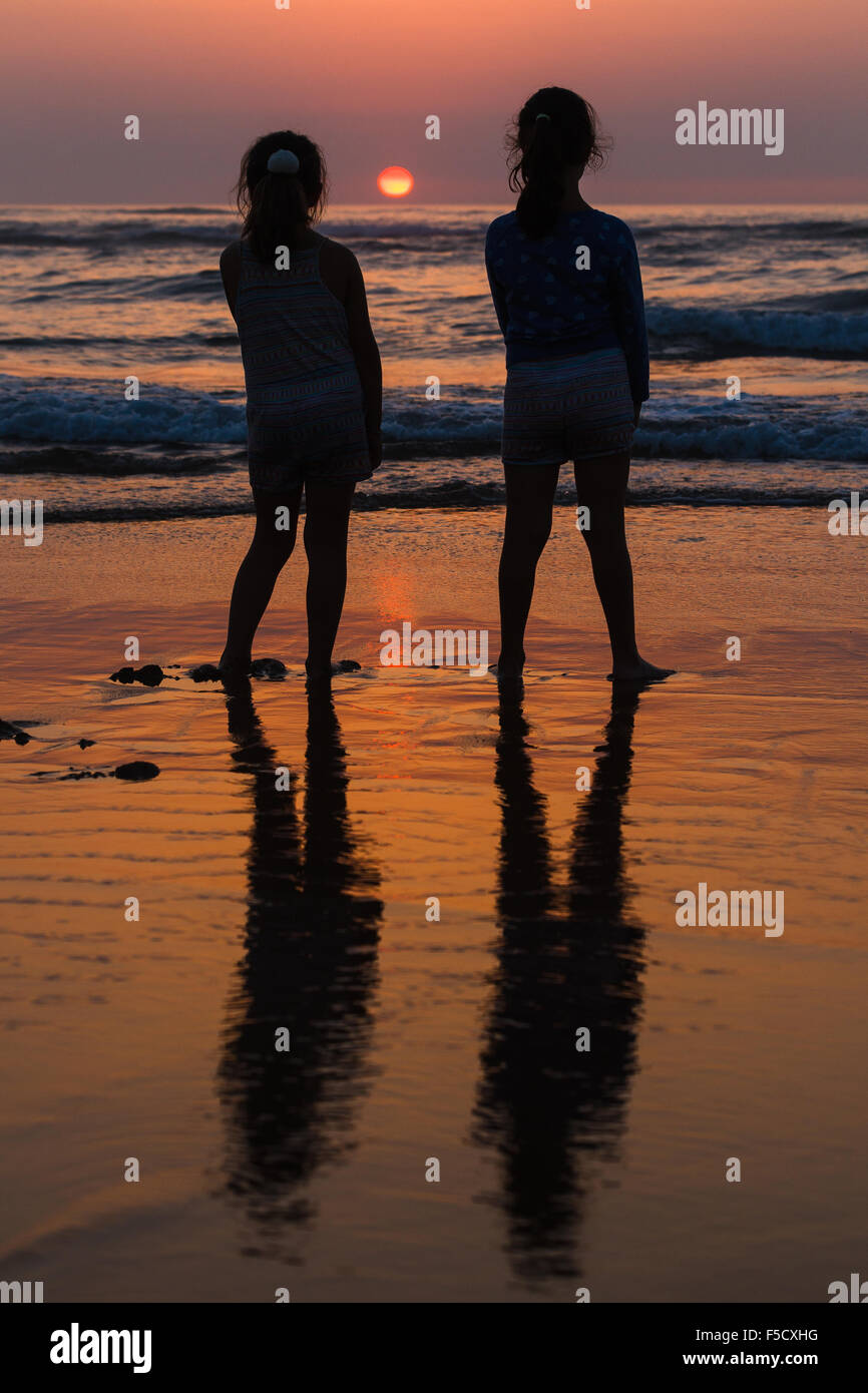 The silhouettes of two girls by the shoreline at sunset, Valdearenas Beach, Liencres, Pielagos. Cantabria, Spain. Stock Photo