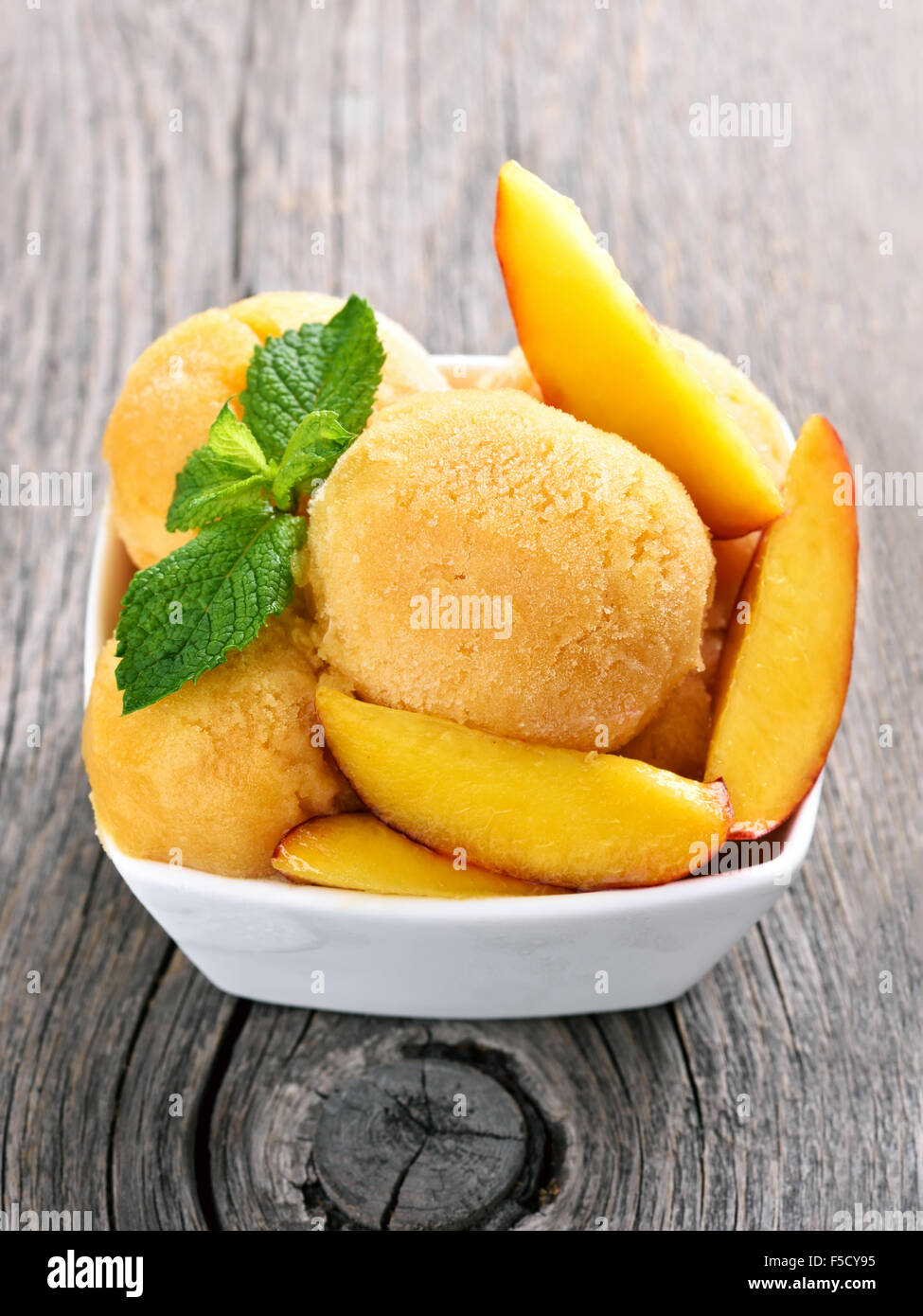 Peach ice cream with mint and slices in bowl on wooden background Stock Photo