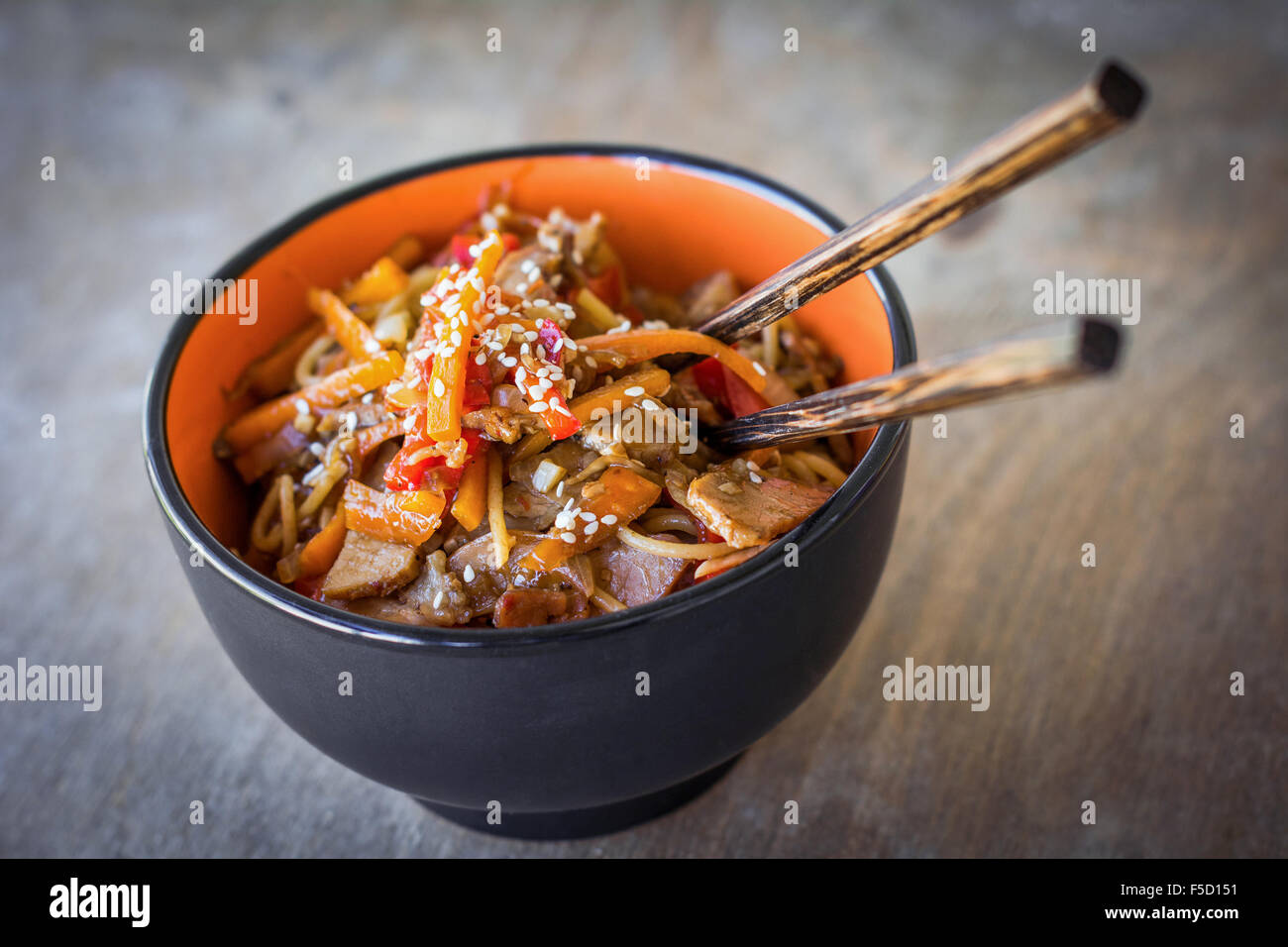 Stir fry with vegetables and meat garnished with sesame seeds in bowl with chopsticks. Traditional asian cuisine Stock Photo