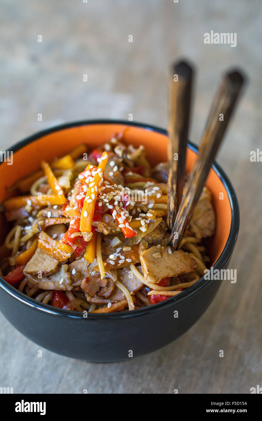 Stir fry with vegetables and meat garnished with sesame seeds in bowl with chopsticks. Traditional asian cuisine Stock Photo