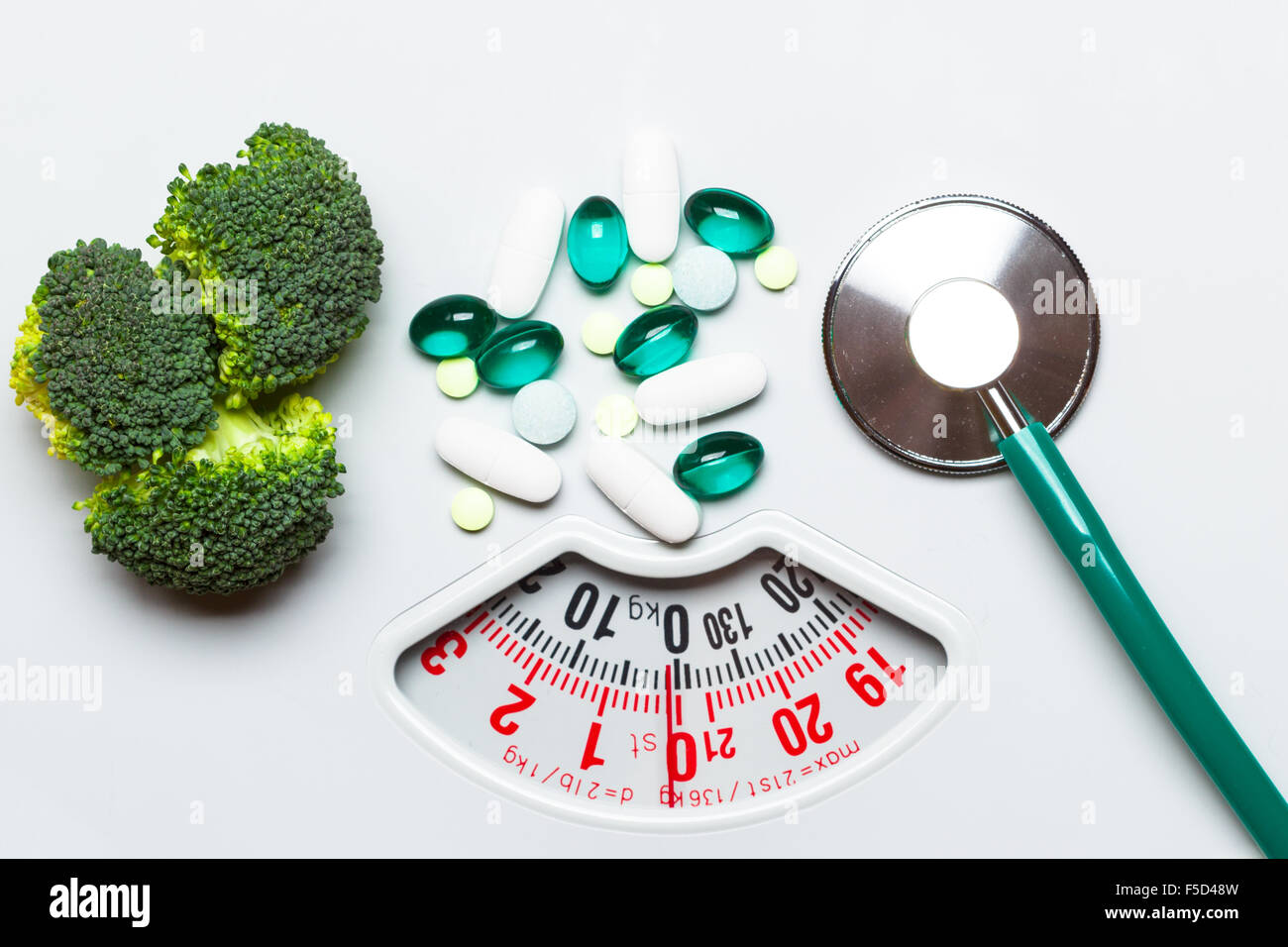 Diet healthy eating weight control and health care concept. Closeup green broccoli stethoscope pills on white scales, choice between Stock Photo