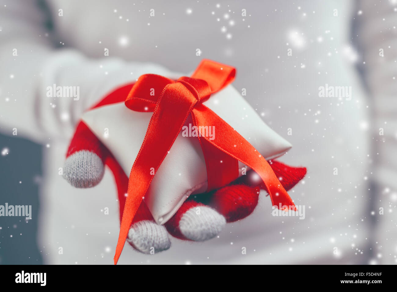 Woman giving Christmas gift wrapped with red ribbon decoration, holiday season with snowflakes falling, retro toned image with s Stock Photo