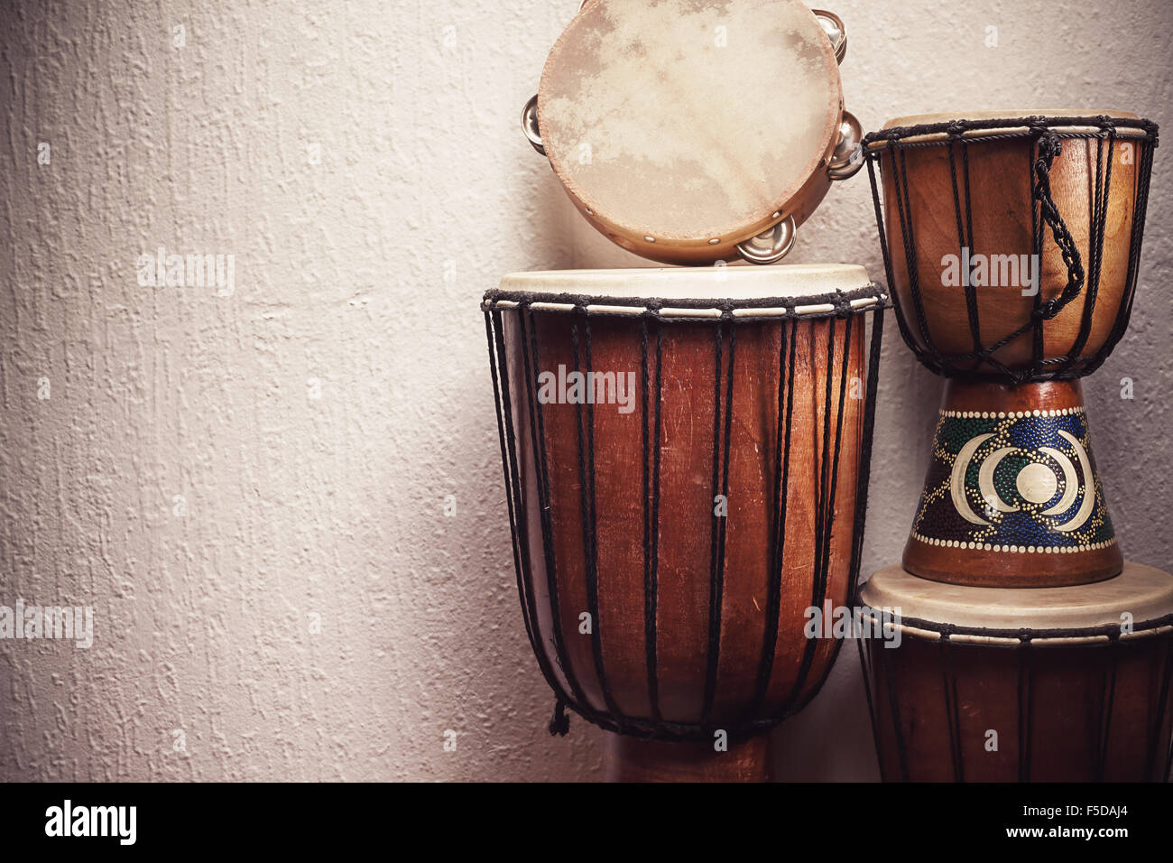 Various djembes and tambourine in front of a rustic wall. Stock Photo