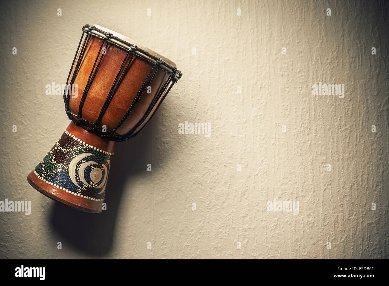One decorated wooden djembe in front of an old rustic wall. Stock Photo