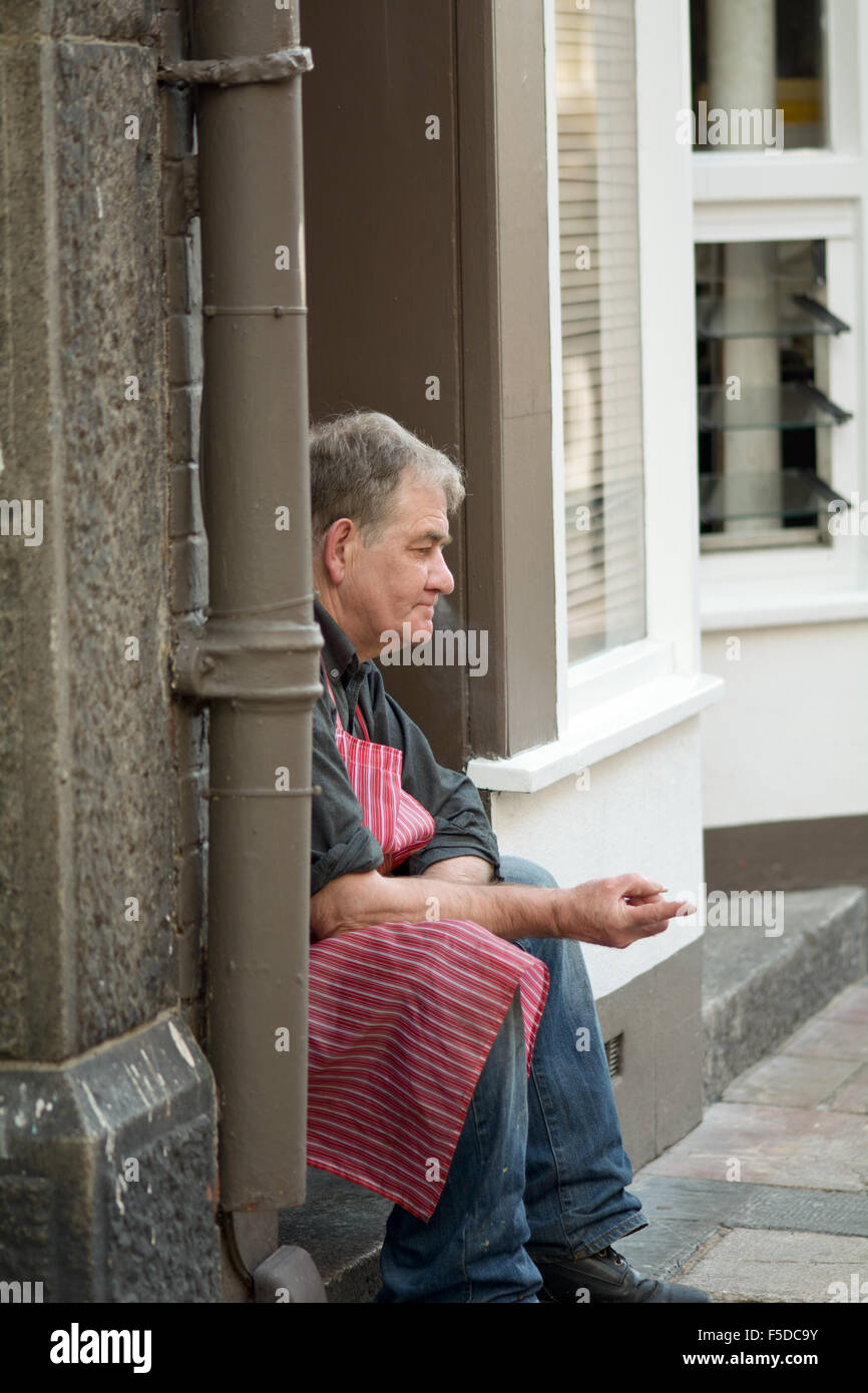Man having a break from work sitting in a doorway smoking a cigarette in Plymouth, Devon, England Stock Photo