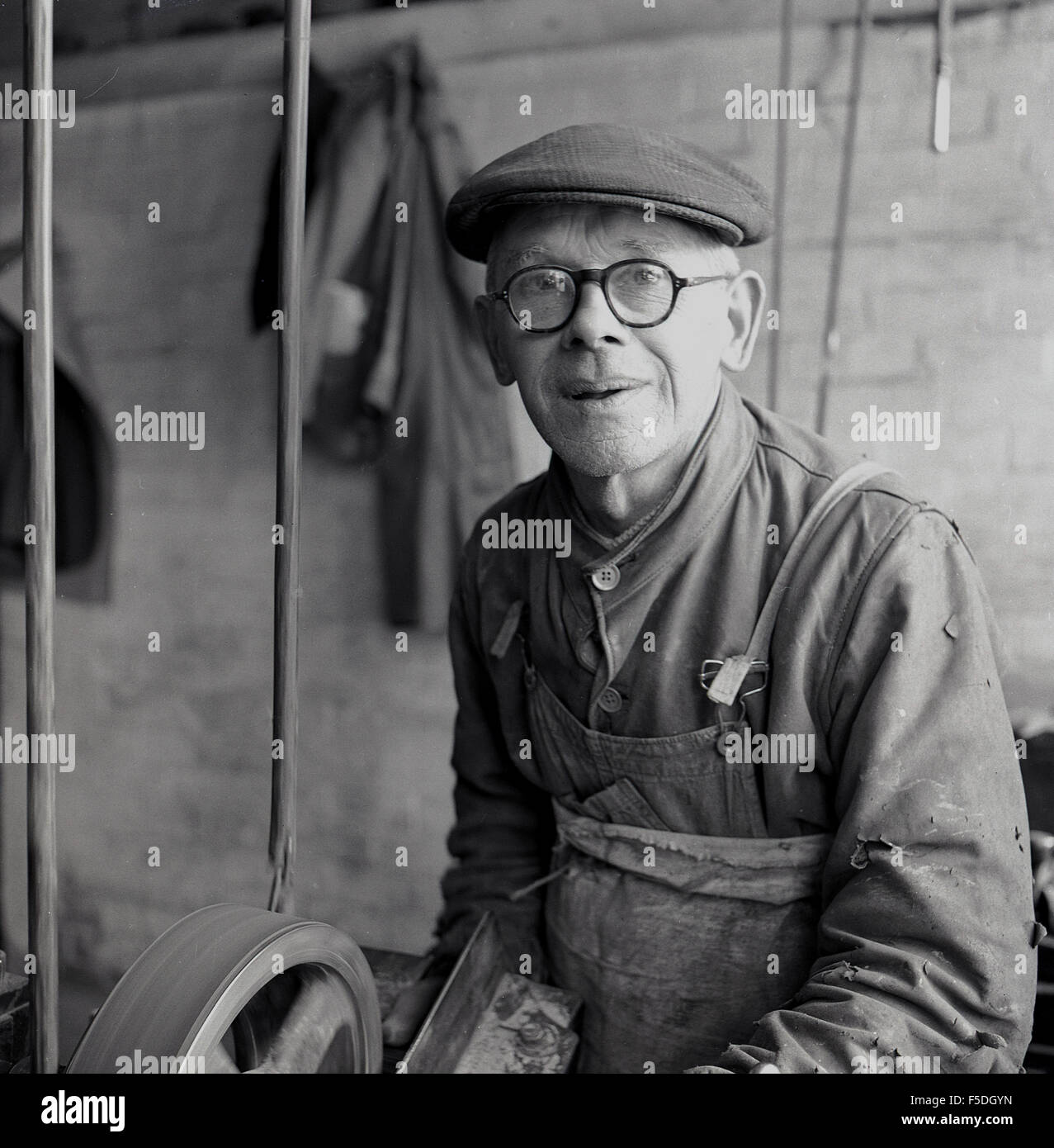 1950s historical picture, elderly working man at his lathe wearing cap