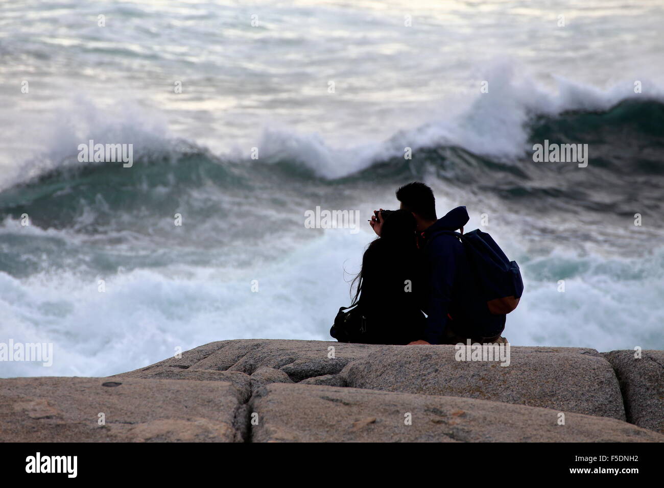 A couple or two people on the rocks at Peggy's Cove, Nova Scotia that are too close to the waves and in danger of drowning. Stock Photo