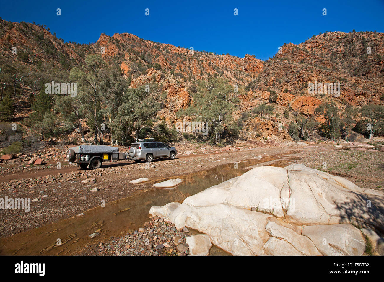 Four wheel drive vehicle towing camper trailer on road through rugged red hills of Flinders Ranges in outback Australia Stock Photo