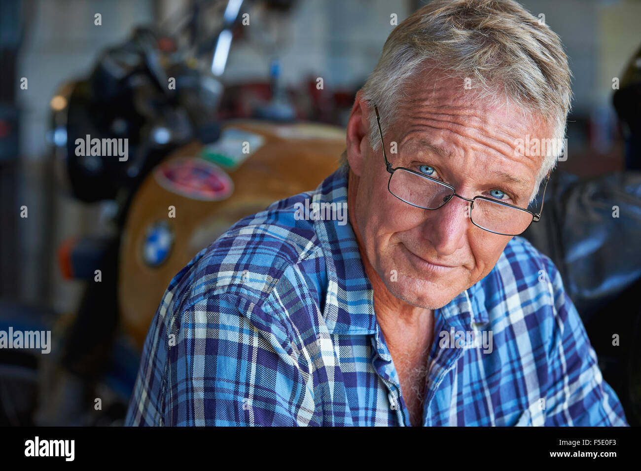 Portrait of a middle aged man and his old motor bike. His tough exterior is softened by his blue eyes and comforting smile. Stock Photo