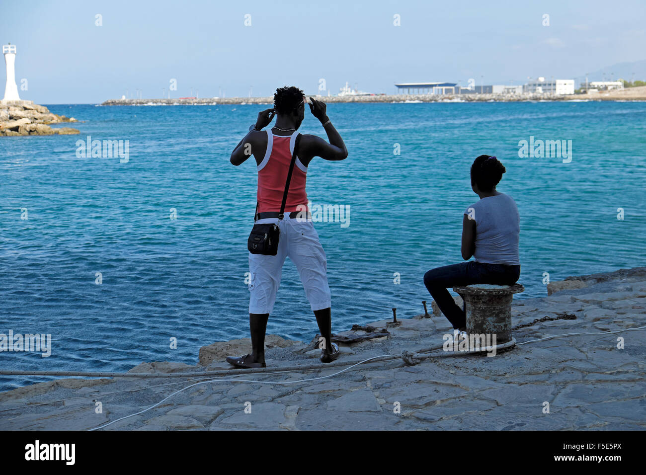 People African couple tourists sitting looking at the sea along the quay at the entrance to Kyrenia Harbour in North Cyprus   KATHY DEWITT Stock Photo