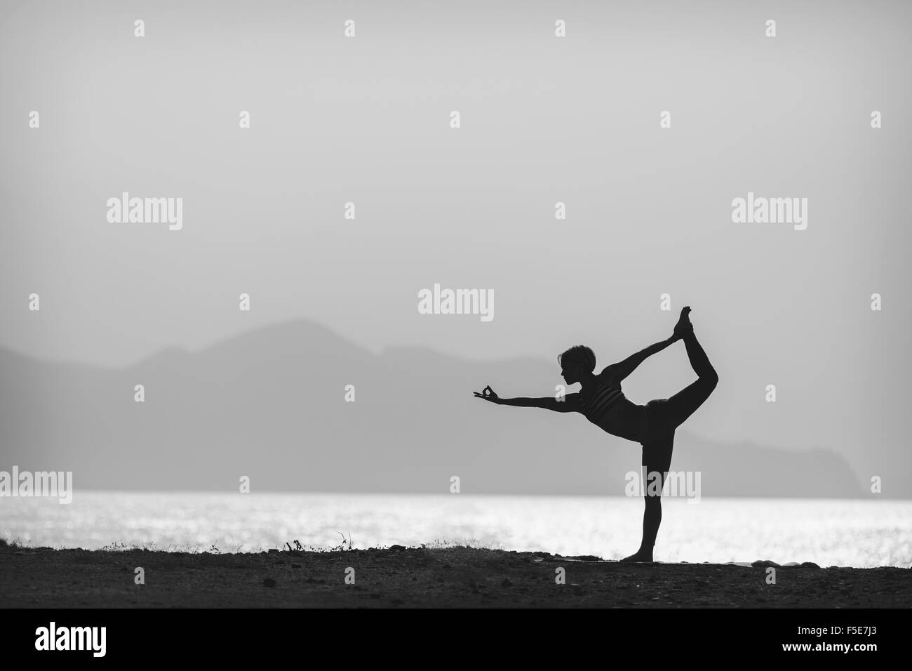 Woman meditating in yoga pose silhouette at the ocean, beach and mountains. Motivation and inspirational exercising. Black and w Stock Photo