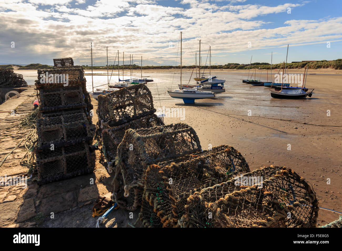 Lobster pots on harbour wall and yachts on beach at low tide on a summer evening, Beadnell, Northumberland, England, UK Stock Photo