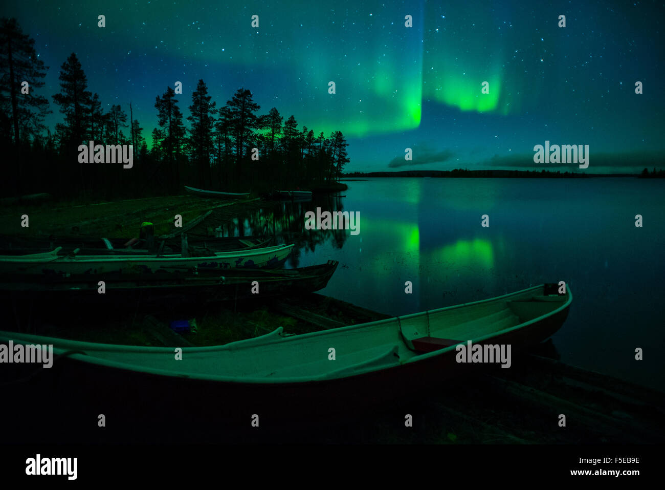 Beached canoes and Aurora Borealis and stars reflected in lake at night, Muonio, Lapland, Finland, Scandinavia, Europe Stock Photo