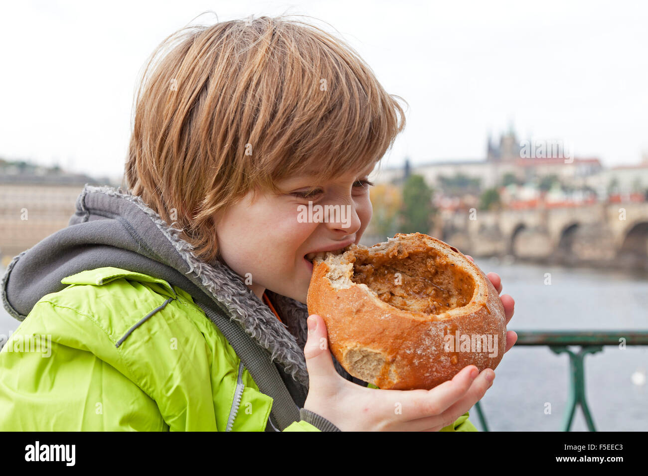 boy eating goulash soup in bread in front of castle and Charles Bridge
