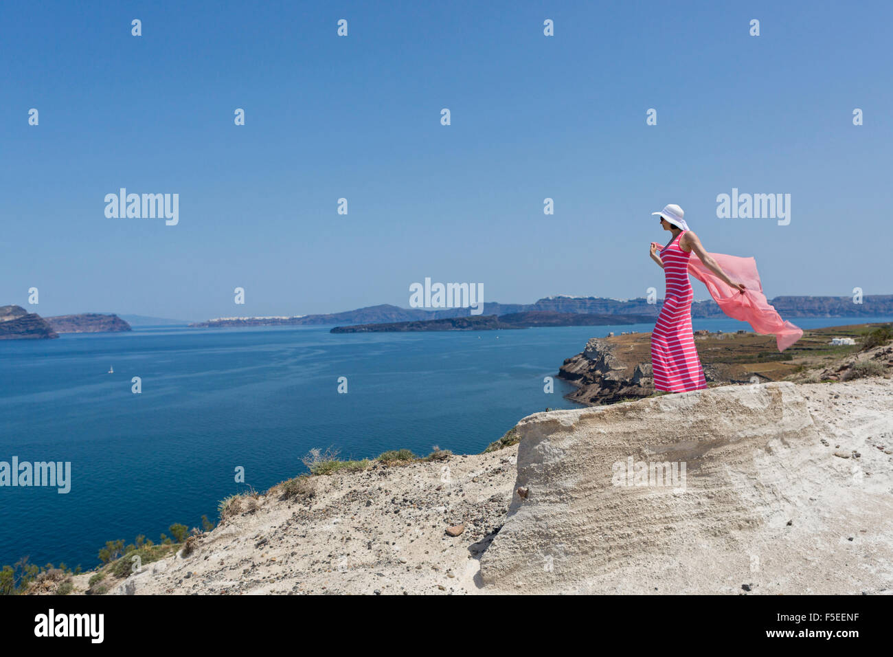 Woman in a long summer dress standing on a cliff and watches the ships ...