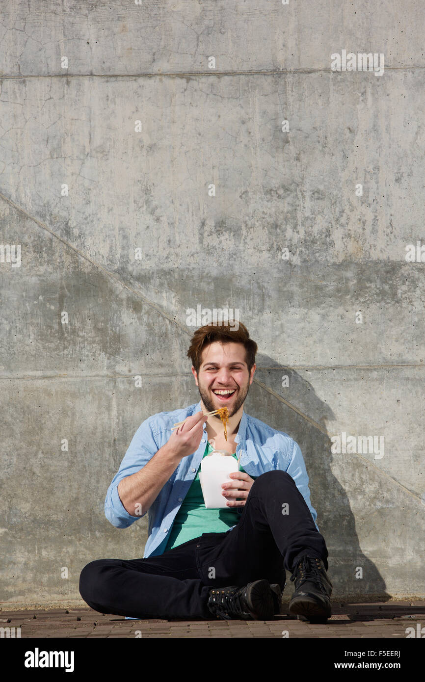 Portrait of a cheerful man eating chinese takeaway food from box with chopsticks Stock Photo