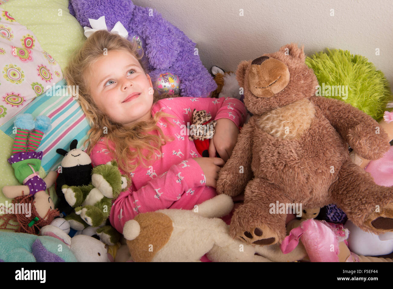 Girl lying on bed, surrounded by cuddly toys Stock Photo