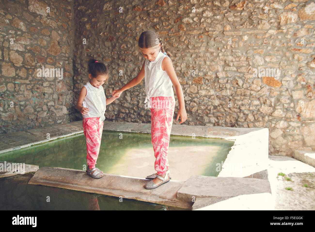 Two girls walking along ledge by a pool of water Stock Photo