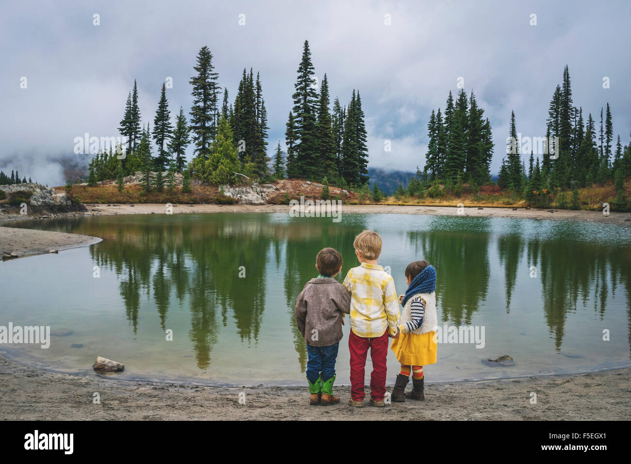 Rear view of two boys and a girl standing by lake Stock Photo - Alamy