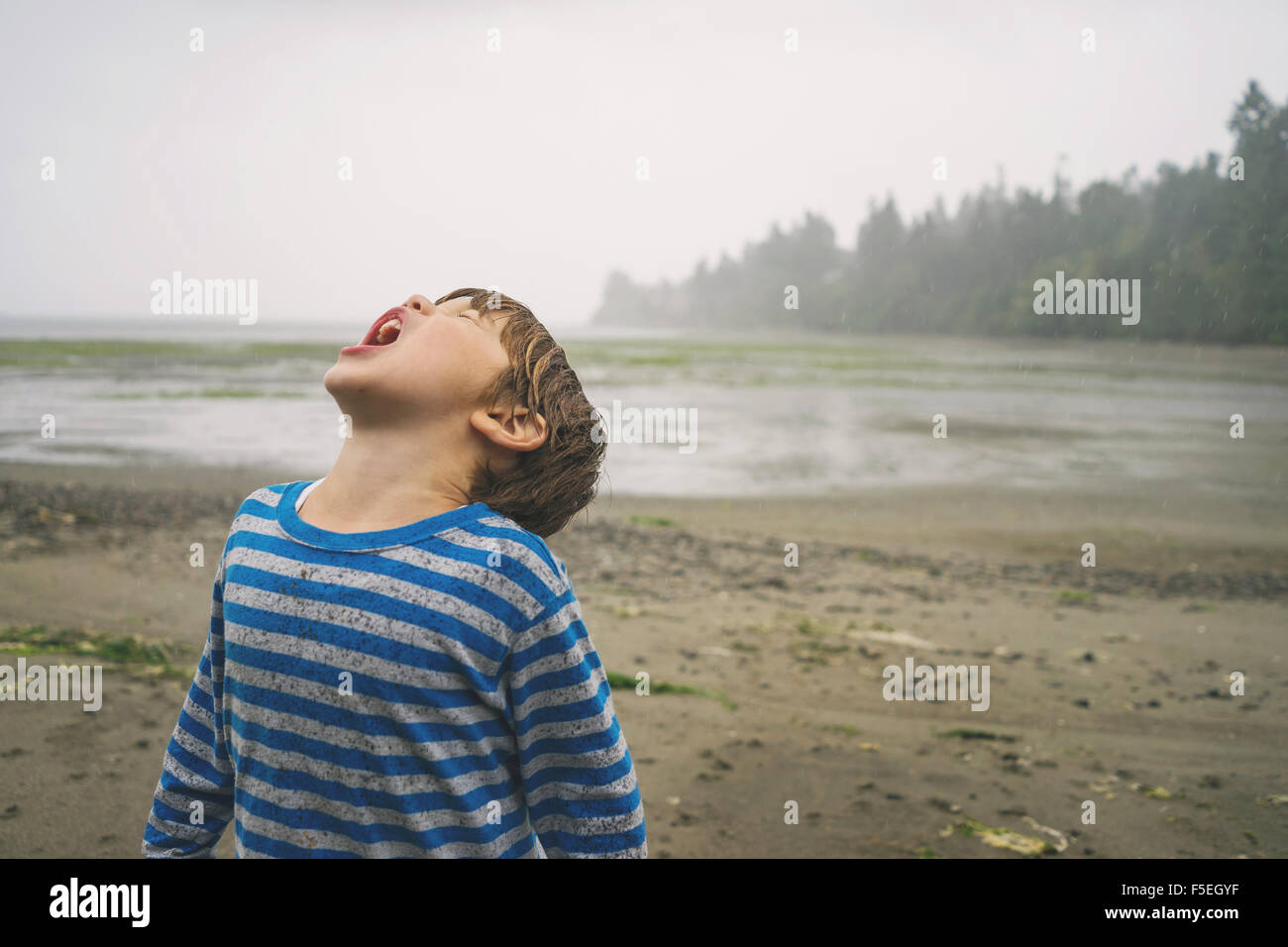 Boy with his head tilted back catching rain in mouth Stock Photo
