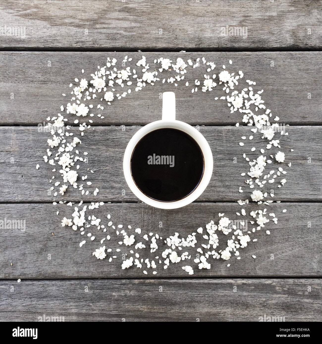 Mug of coffee surrounded by a circle of white flower petals Stock Photo