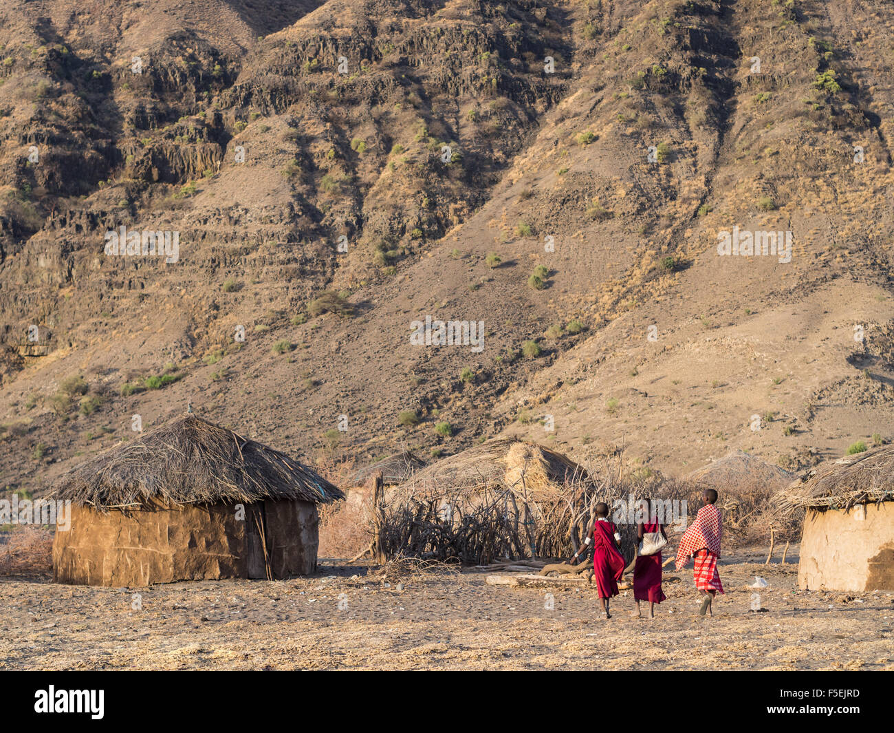 Three kids walking in a Maasai village in front of the Ol Doinyo Lengai in Arusha Region, Tanzania, Africa, at sunrise. Stock Photo
