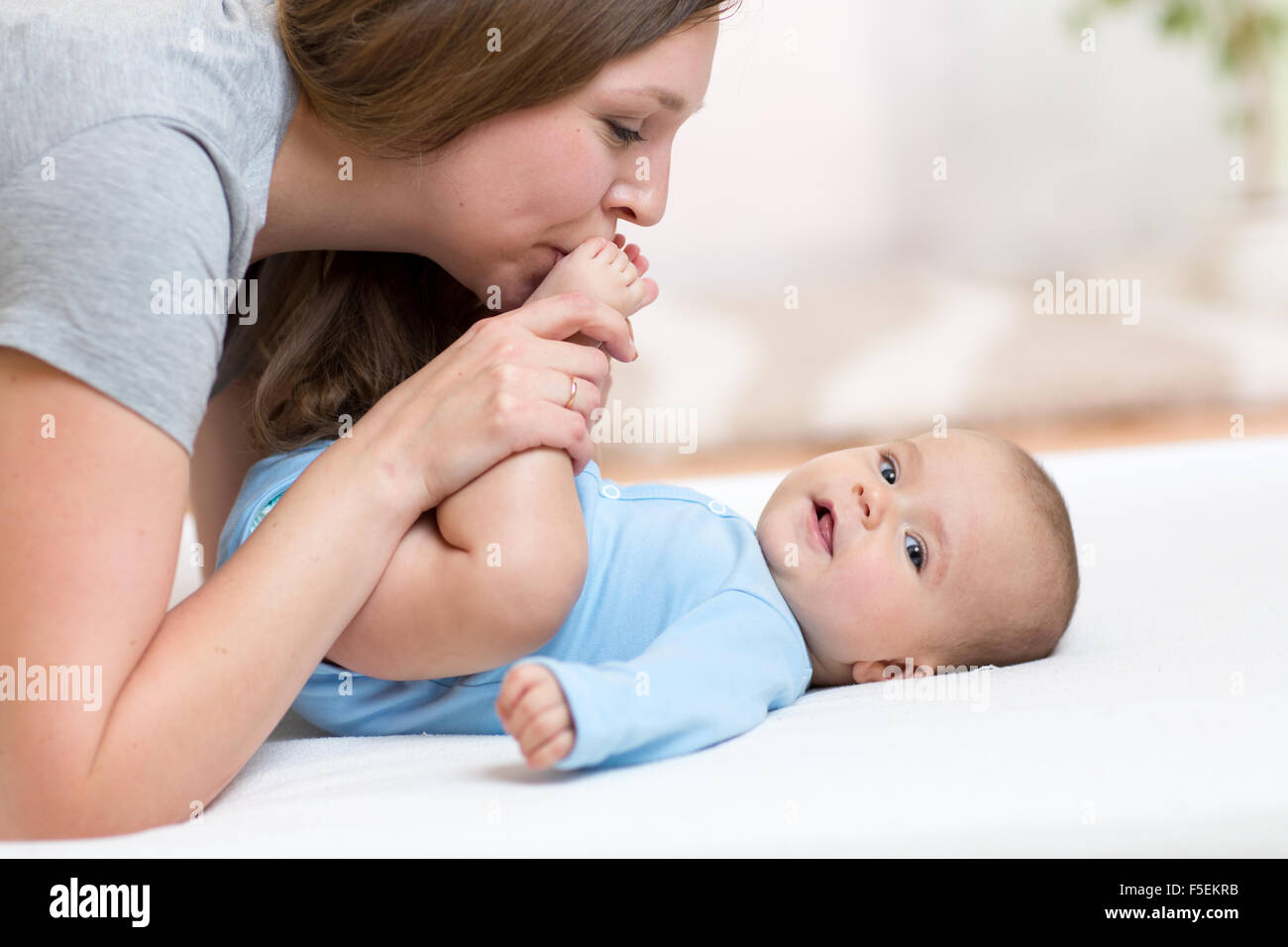 Mother kisses baby daughter feet while playing on a white bed Stock Photo