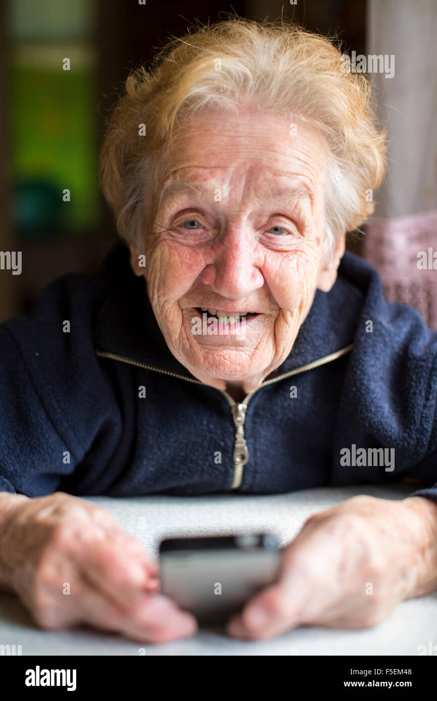 Old woman is typing on phone sitting on the table. Stock Photo